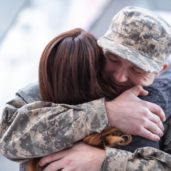 Man hugging his wife after returning home from service A handsome man dressed in a military uniform passionately hugs his partner as he greets her returning from his military service in this close-up.